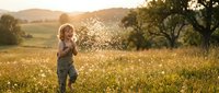 Young blonde girl with fair complexion, approximately 3-5 years old, blowing dandelion seeds in a sunlit meadow during golden hour. Ideal for parenting, childhood, and nature themes.