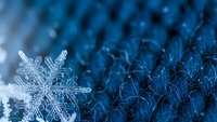 Single snowflake with intricate crystalline structure on blue textured winter surface with frost patterns for seasonal holiday designs.