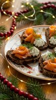 Festive salmon canapes with cream cheese and dill on dark bread served on elegant plate with Christmas decorations and warm lights for holiday entertaining.
