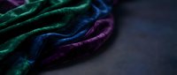 Crumpled velvet fabric in jewel tones of emerald, sapphire, and amethyst draped on dark surface. Suitable for luxury, fashion, textile, and design projects.