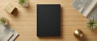 Black hardcover book mockup on wooden desk with air plants, kraft boxes and linen fabric for branding design projects.