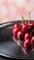 Fresh red cherries with water droplets on dark plate against soft pink blurred background for culinary and food photography projects.
