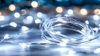 Glowing LED string lights creating magical bokeh effect against dark background, soft focus fairy lights illuminate with cool white glow for festive decoration.
