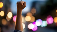 Raised fist silhouette against blurred city lights at night symbolizing strength, protest, victory and determination in urban environment.