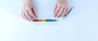 Hands arranging colorful beads in a row on white background using tweezers, top view flat lay for science, education or craft concept.