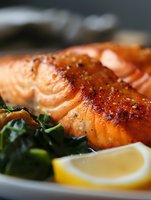 Grilled salmon fillet with crispy skin served on a bed of sautéed spinach with lemon wedge, close-up view of gourmet seafood dinner.