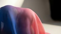 Soft fabric draped in gradient lighting transitions from cool blue to warm pink tones, creating an abstract play of color and shadow on translucent material.