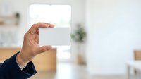 Close-up of hand holding blank white card in modern bright interior space, suitable for business branding and marketing mockups.