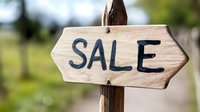 Rustic wooden arrow sign with Sale text painted in dark letters against natural bokeh background, mounted on wooden post for retail and marketing promotions.