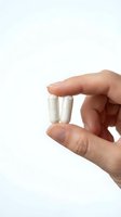 Hand holding two white capsules pills between fingers on clean white background for healthcare and medical supplement concepts.