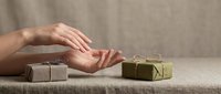 Female hands reaching for eco-friendly wrapped gift boxes on neutral linen surface, sustainable packaging concept for holidays and special occasions.