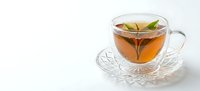 Fresh herbal tea in elegant glass cup with green leaves on crystal saucer, isolated on white background for wellness and beverage design projects.
