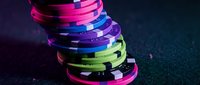 Colorful neon casino poker chips stacked in vibrant pink, purple, blue and green lights creating dramatic gaming atmosphere for entertainment design.