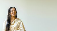Young woman with braided hair and South Asian ethnicity wearing gold satin shirt, smiling against neutral background. Suitable for lifestyle, fashion, beauty, and diversity marketing campaigns.