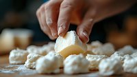 Hands kneading and shaping fresh homemade dough into small portions on wooden surface dusted with flour, close-up view showing cooking process and texture.