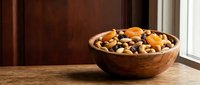 Wooden bowl filled with mixed nuts and dried fruits on rustic table by window. Healthy snacking, organic food concept for kitchen and dining designs.