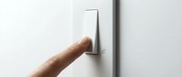 Caucasian hand pressing a modern white light switch with a small green eco leaf icon on a clean white wall, energy saving concept.