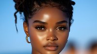 Young African American woman with natural curly hair updo against blue sky background, glowing skin, minimal makeup, and gold hoop earrings in summer portrait.