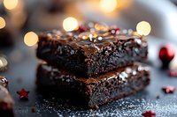 Homemade dark chocolate brownies with rich fudgy texture and glossy ganache topping stacked on dark surface with festive bokeh lights and red decorations.
