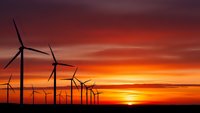 Wind turbines silhouetted against dramatic sunset sky with orange and purple clouds generating clean renewable energy for sustainable power production.