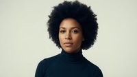Professional African American woman with natural afro hairstyle wearing black turtleneck sweater against neutral background for business and lifestyle concepts.