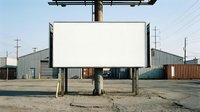 Blank vintage drive-in movie theater screen in abandoned industrial area with metal warehouses and utility poles, suitable for advertising mockups.