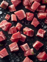 Fresh raw tuna cubes with water drops and herbs scattered on dark background, top view composition for seafood restaurant menu and food photography.