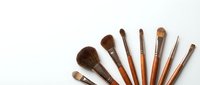 Set of professional makeup brushes with wooden handles arranged on white background, top view with copy space for beauty and cosmetic design.