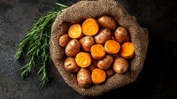 Fresh raw organic carrots and potatoes in rustic burlap sack on dark background with dill herbs, top view. Natural farm vegetables for healthy cooking.