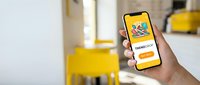 Hand holding smartphone with colorful sneaker shopping app on screen, bright yellow interior background, mobile commerce concept.