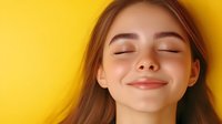 Young Caucasian woman with closed eyes and gentle smile expressing joy and serenity against vibrant yellow background, radiating happiness and positive emotions.