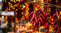 Red chili peppers hanging in bunches at festive market with warm bokeh lights creating cozy holiday atmosphere for culinary and seasonal cooking themes.