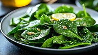 Fresh spinach salad with lemon and pine nuts served on dark plate, closeup view of healthy green leaves garnished with seeds and citrus dressing.
