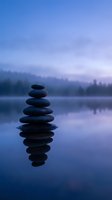 Zen stone stack balanced on calm lake water with perfect reflection during twilight hour creating peaceful meditation atmosphere for wellness concepts.