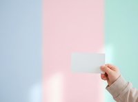 Caucasian hand holding blank white card against soft pastel background with blue, pink, and mint green color blocks for mockup and branding purposes.
