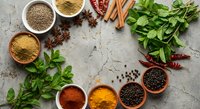 Aromatic spices and fresh herbs arranged in wooden bowls on rustic stone surface for culinary cooking and seasoning recipes.
