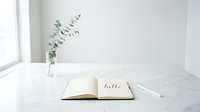 Open notebook with hello lettering on marble surface, eucalyptus branch in glass vase, minimalist white interior, clean workspace.