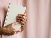 Mature man with brown skin holding blank white book against pink background, suitable for education, publishing, and learning concepts.