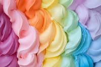 Colorful swirled meringue or whipped cream texture in rainbow pastel shades of pink, orange, yellow, mint green, purple and blue creating soft wavy pattern.