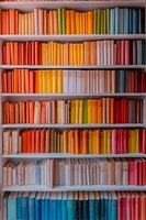 Colorful books arranged by spectrum on wooden shelves creating rainbow pattern in library. Books spines in orange, yellow, blue and red shades form gradient display.