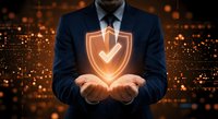 Professional businessman in dark suit holding glowing orange shield with checkmark symbol representing cybersecurity protection and data safety solutions.