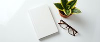 Minimalist workspace with blank notebook, eyeglasses and snake plant on white background. Clean desk setup for productivity and planning concepts.