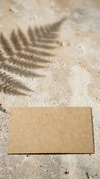 Blank kraft paper card on sandy beach with fern leaf shadow, ideal for business branding, stationery design, and summer marketing campaigns.