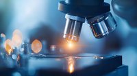 Close-up of microscope lenses with glowing light illuminating glass slide in laboratory setting, scientific research equipment in blue tones.