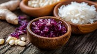 Fermented red cabbage sauerkraut in wooden bowl with white cabbage, ginger and garlic on rustic table for healthy probiotic nutrition and cooking.