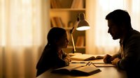 Father helping young daughter with homework at wooden desk under warm lamp light creating cozy evening study atmosphere for family education concepts.