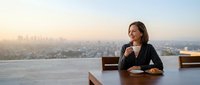 Professional businesswoman enjoying morning coffee on rooftop terrace overlooking city skyline at sunrise, corporate lifestyle and urban living concept.