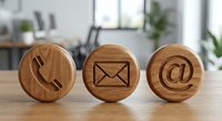 Wooden contact icons on desk showing phone, email and at symbol for business communication and customer service in modern office environment.