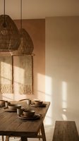 Warm minimalist dining room with woven pendant lights, rustic wooden table, ceramic dinnerware and macrame wall hanging in natural earth tones.