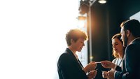 Business professionals networking at corporate event with warm lighting and handshake interaction for professional communication and partnership concepts.